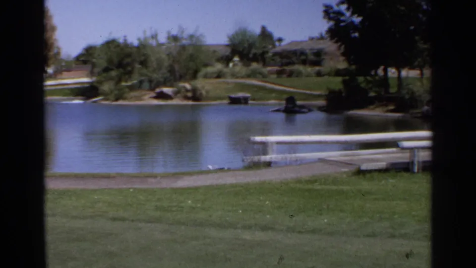 Scottsdale golf course view showing a water hazard, white rail, green grass, shade trees, and residential buildings beyond the course.