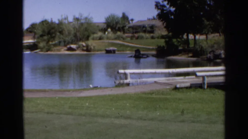 1968 Scottsdale golf-course pond with trimmed grass, benches, rocks, trees, and low buildings in a soft 8mm frame.