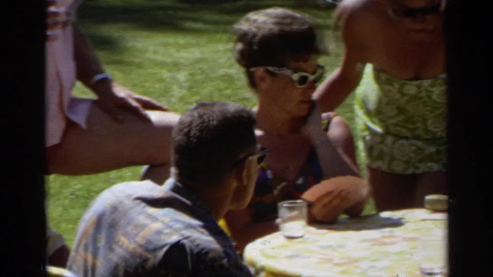 1968 Scottsdale home-movie frame showing adults around a round lawn table, with drinks and casual summer clothing visible.