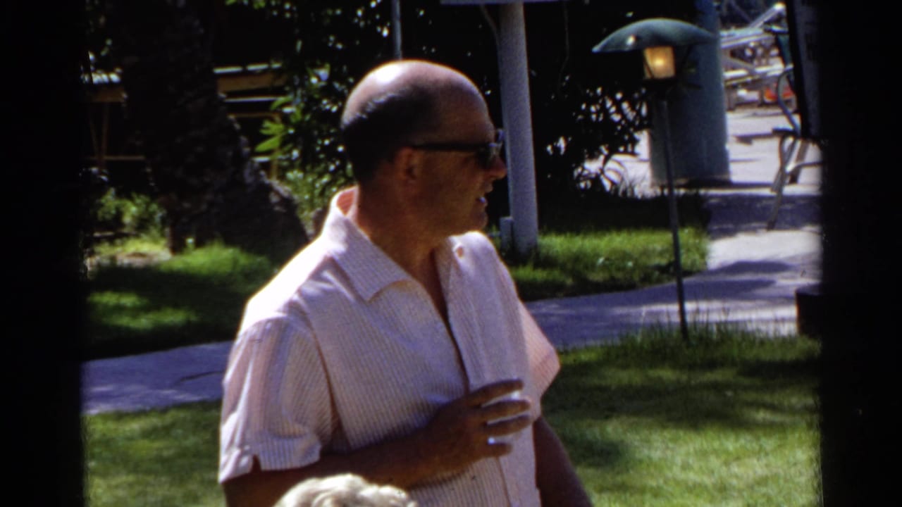Man in sunglasses holding a drink in a sunny backyard.