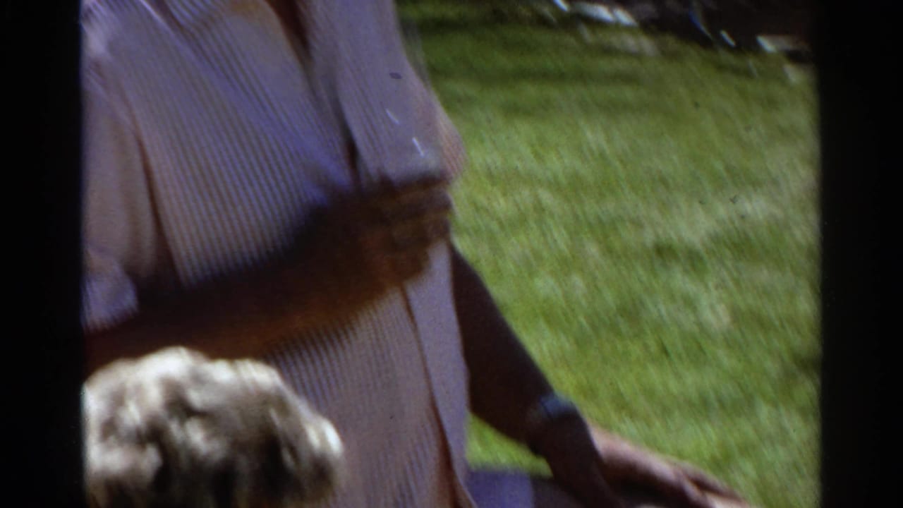 Partial view of an adult in a striped shirt standing on a sunny lawn.