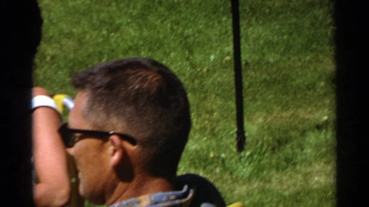 Adults seated outdoors on grass, with a man in sunglasses in the foreground.