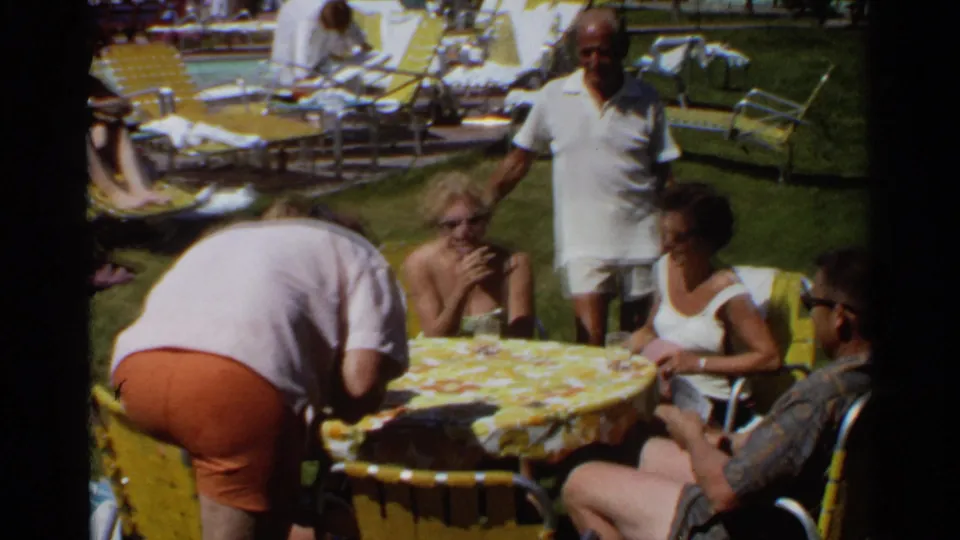 1968 Scottsdale frame showing adults around a yellow-covered lawn table as one person bends forward during the card game.