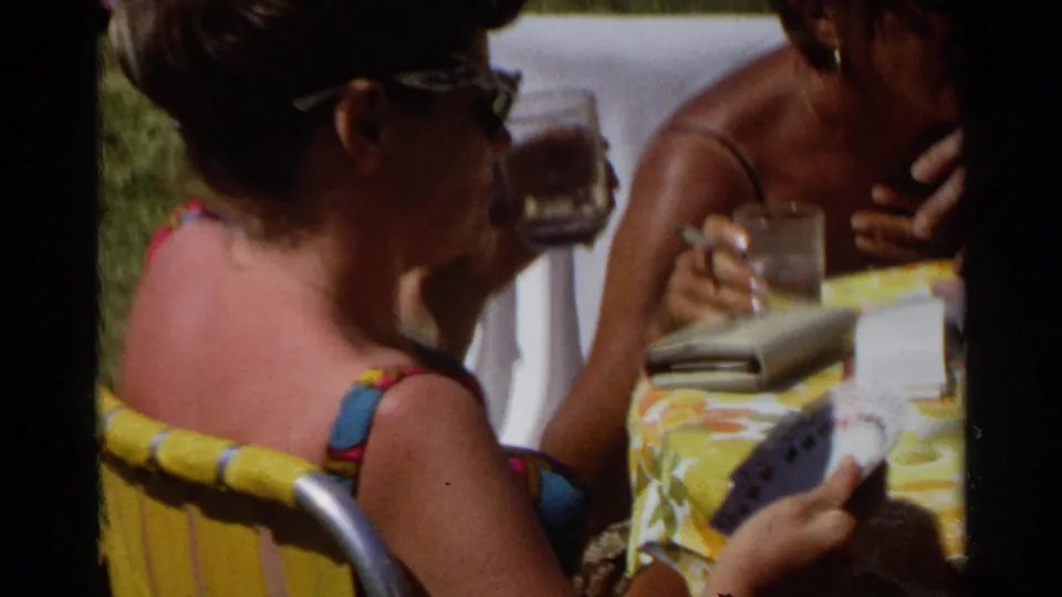 A close 8mm view shows women in sunglasses at the Scottsdale table, with drinking glasses, cards, and a small case visible.