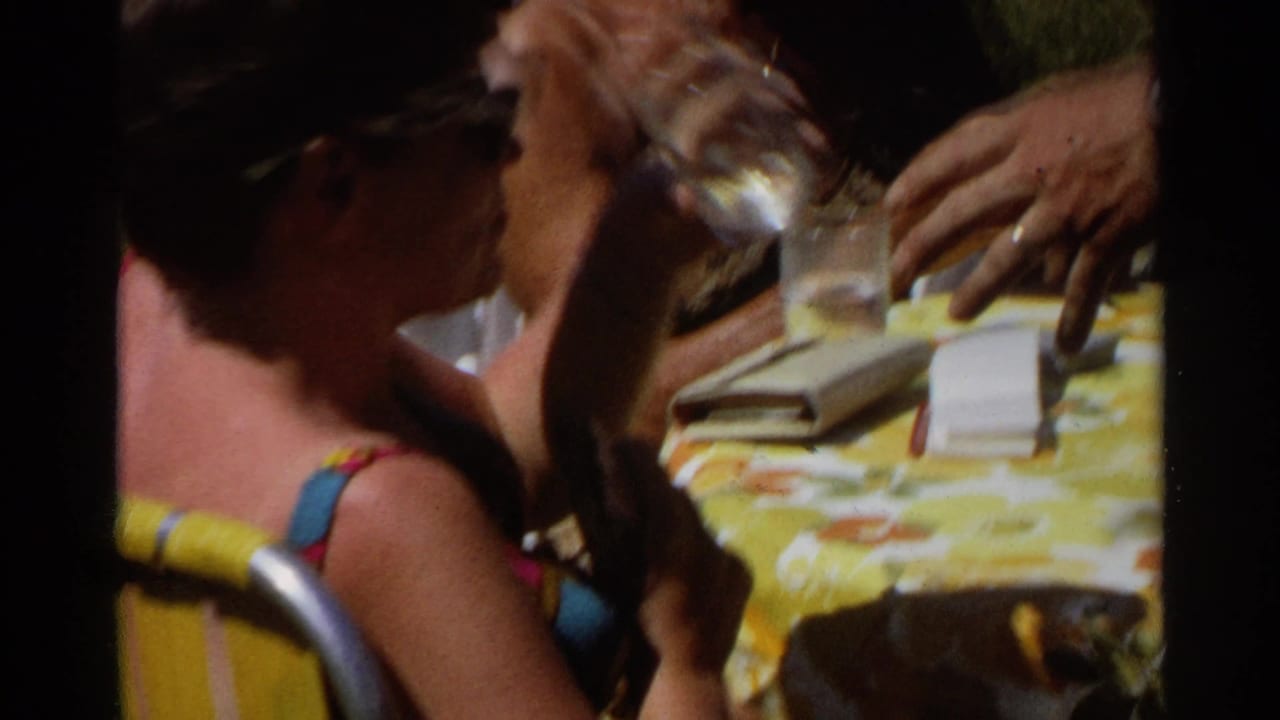 Adults seated around a yellow floral tablecloth with drinks in bright sun.