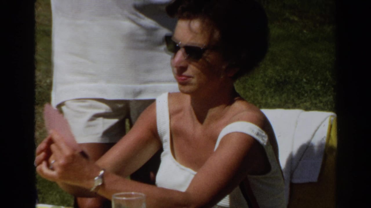 Woman in sunglasses sits outdoors holding a pink card at a table.