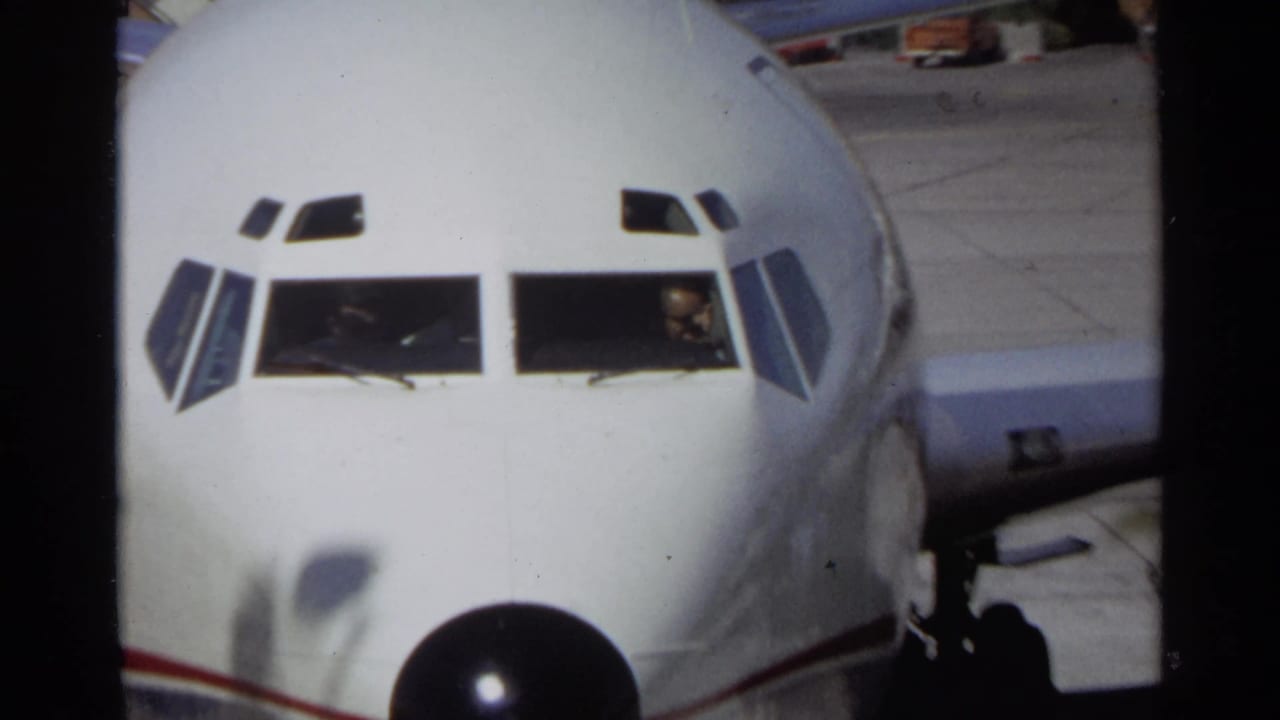 Close view of a white airplane nose with cockpit windows and a black nose cone on the tarmac.