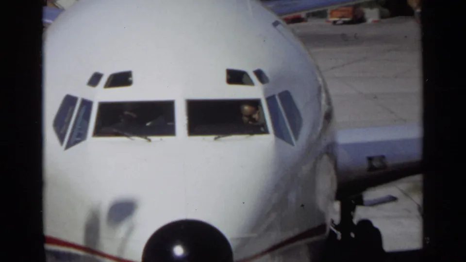 1968 Scottsdale home-movie frame showing a close front view of a white airplane with red striping, cockpit windows, and a black nose cone.