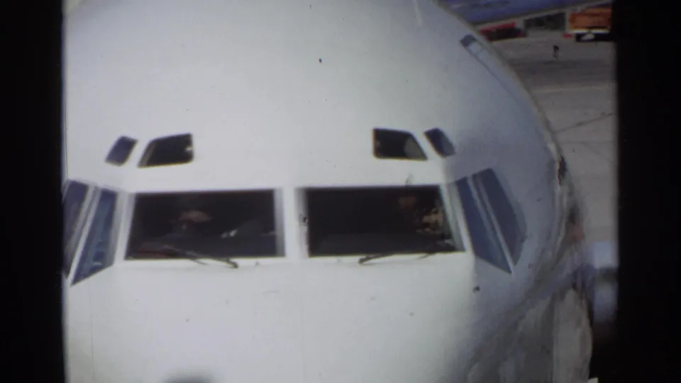 Front-facing 1968 Scottsdale view of the white aircraft nose, cockpit windows with crew visible, and airport pavement in the background.