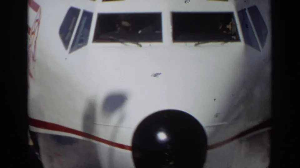 Tight 1968 Scottsdale frame of the airplane nose with black nose cone, red side stripe, and cockpit windows seen from the ramp.