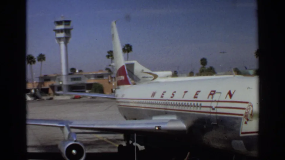Side view of the parked Western Airlines jet at Scottsdale with a control tower, palm trees, and airport buildings in the background.