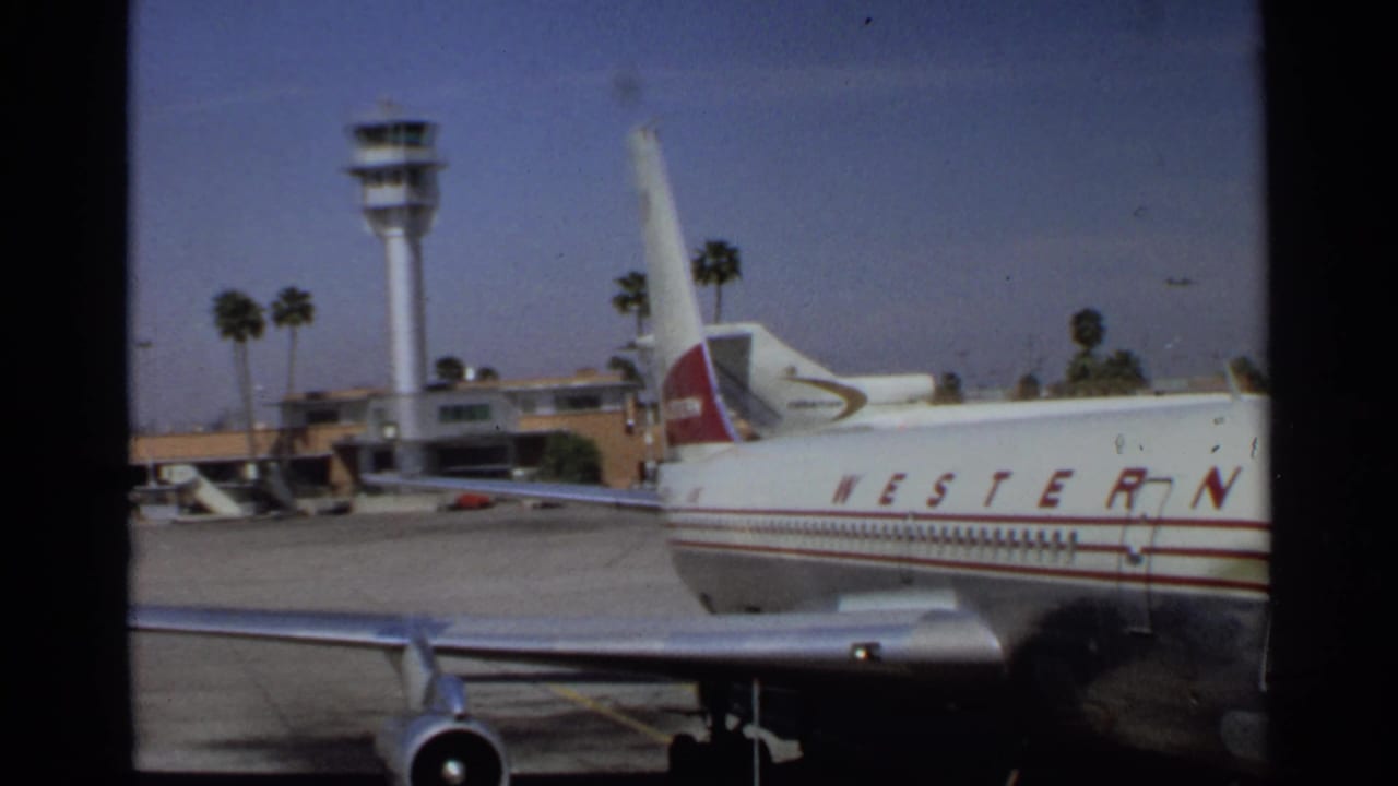 Western Airlines jet parked near a control tower and palm trees at an airport.
