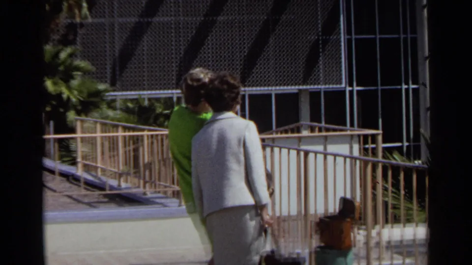 Two women move along a ramp at the Scottsdale airport, framed by railings, palm landscaping, and terminal windows.