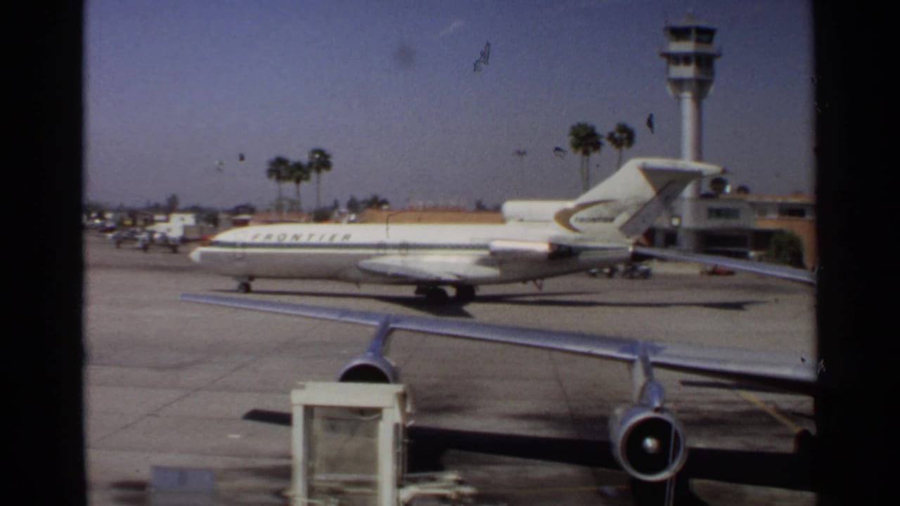 Frontier jet on an airport tarmac seen through a terminal window.