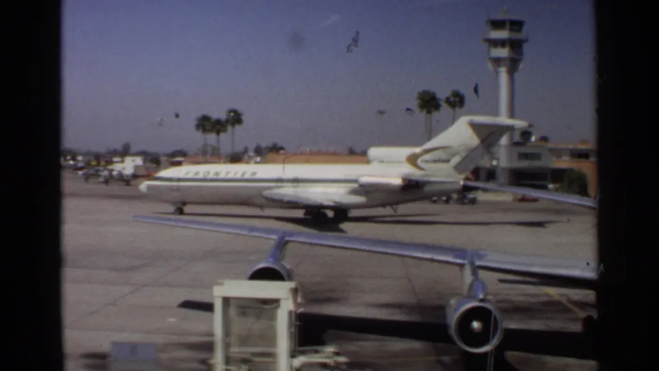 1968 Scottsdale airport view of a Frontier-marked tri-jet on the tarmac, with wing foreground, control tower, and palm trees.