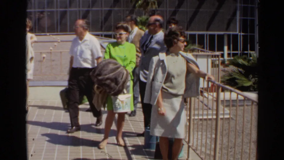 A wider 1968 Scottsdale view shows formally dressed adults moving along a tiled walkway near railings, fencing, and palm landscaping.