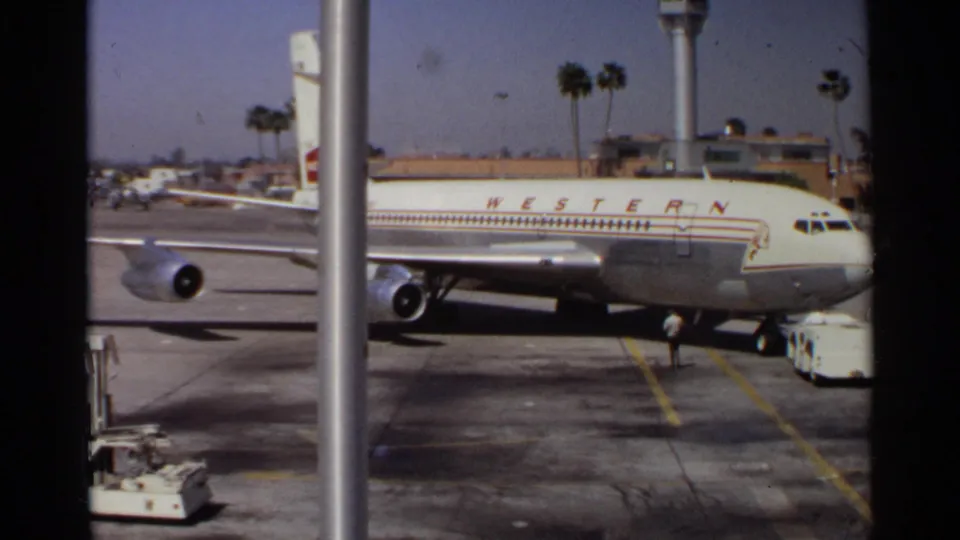 Western Airlines jet remains parked at the tarmac, with a service cart and control tower visible in the Arizona airport background.
