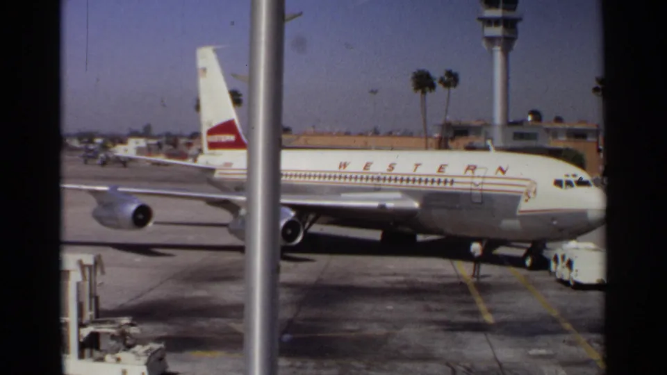 Home-movie view of a Western Airlines jet on the Scottsdale-area tarmac, partially blocked by terminal window supports.