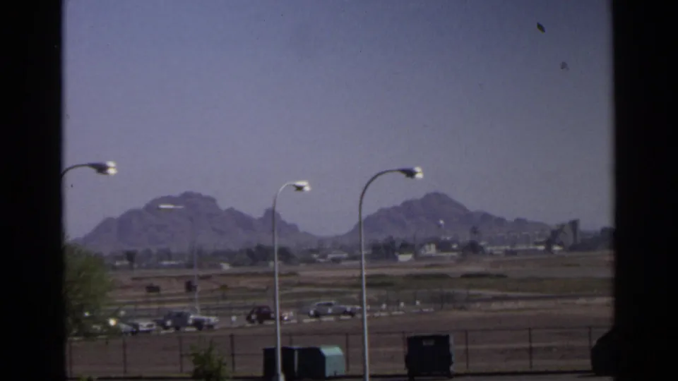 Arizona desert landscape view with road traffic, airport fencing, light poles, and hazy mountains in the distance.
