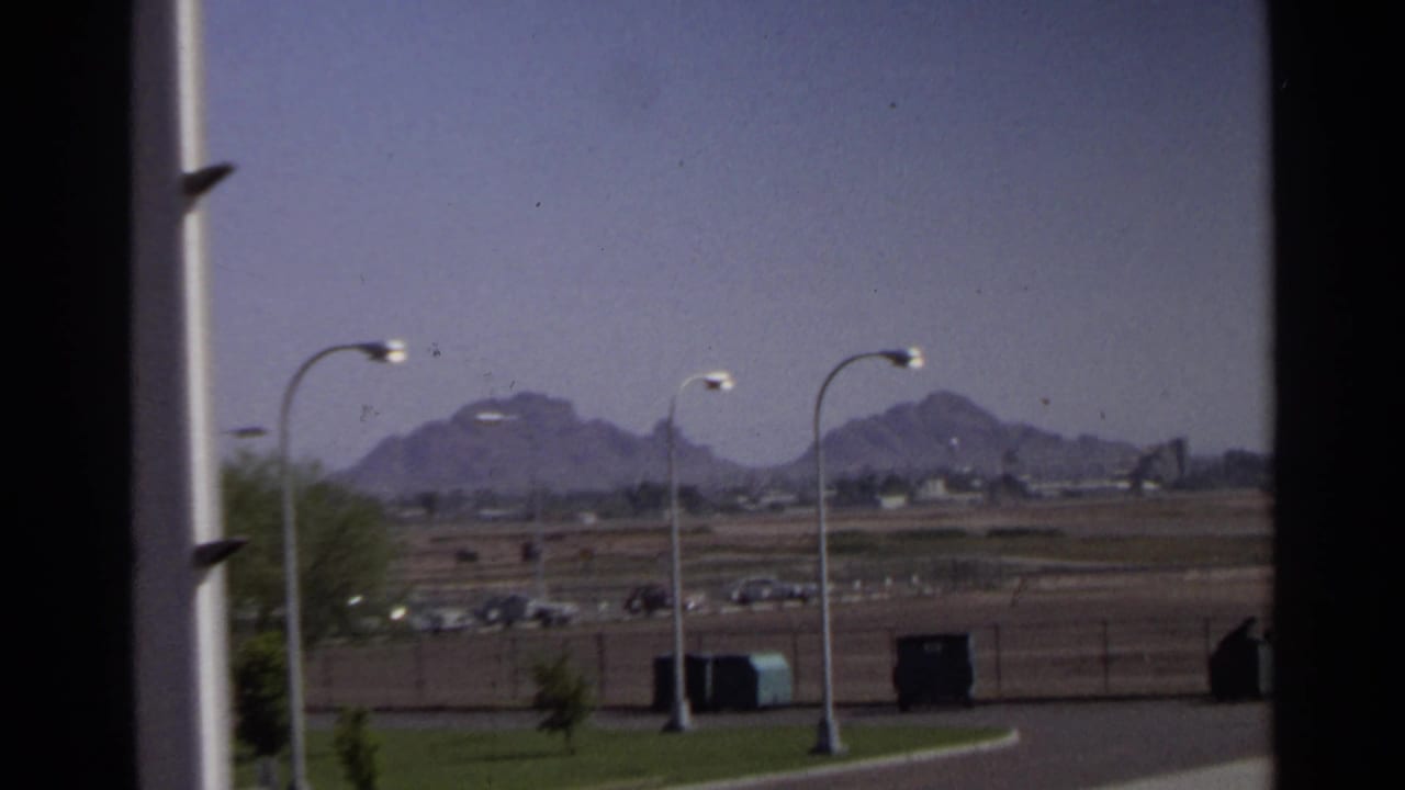 1968 Scottsdale-area view with Camelback Mountain in the distance, roadside lights, green landscaping, and parked cars.