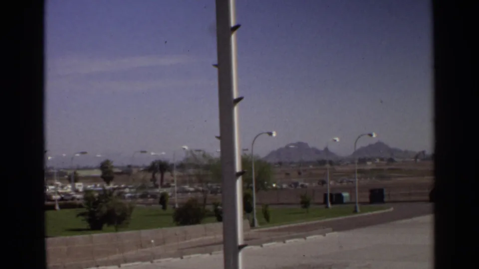 1968 Scottsdale travel view with palm trees, green lawns, parked cars, streetlights, and distant mountains.