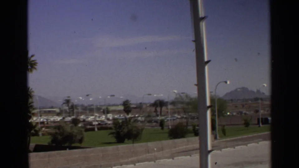 Scottsdale, Arizona roadside landscape from 1968 with parked cars, palms, streetlights, and distant mountain forms.