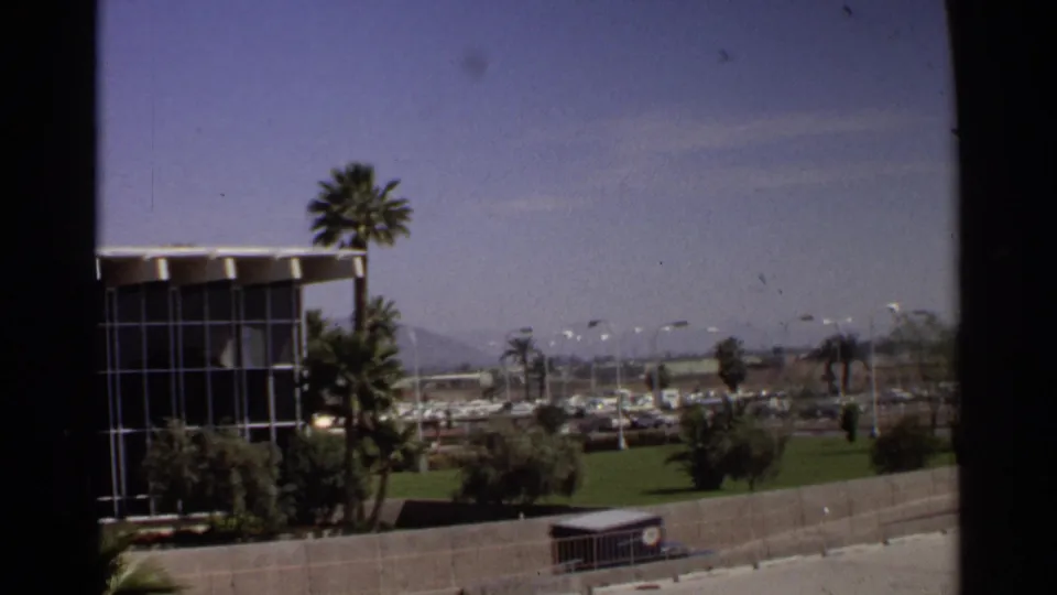 1968 Scottsdale street scene showing a mid-century glass-fronted building, tall palms, green landscaping, parked cars, and distant mountains.