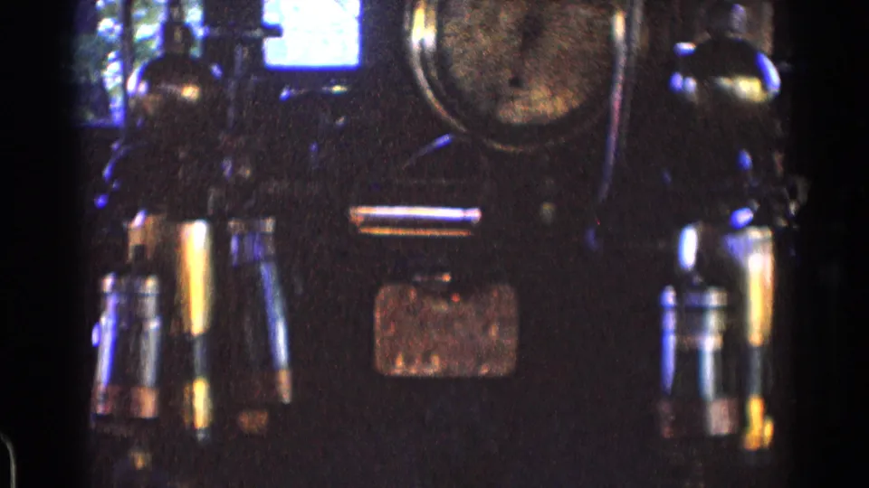 Grainy close-up of train cab equipment in the stated 1976 Chicago footage, with levers, gauge faces, a placard, and bright window glare.