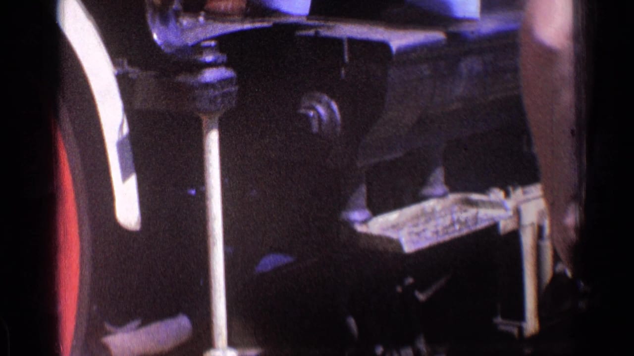 Dark locomotive undercarriage detail with metal lever, fittings, and shadowed machinery.
