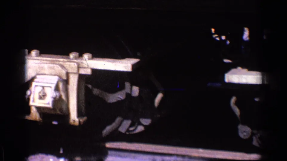 Close 8mm view of a locomotive axle box, rods, and lower frame above rails in 1976 Chicago footage.