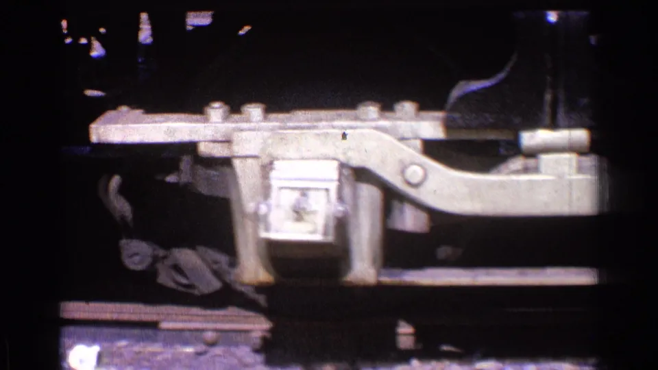 Detailed close-up of bolted locomotive undercarriage hardware and track in archival Chicago 1976 8mm footage.