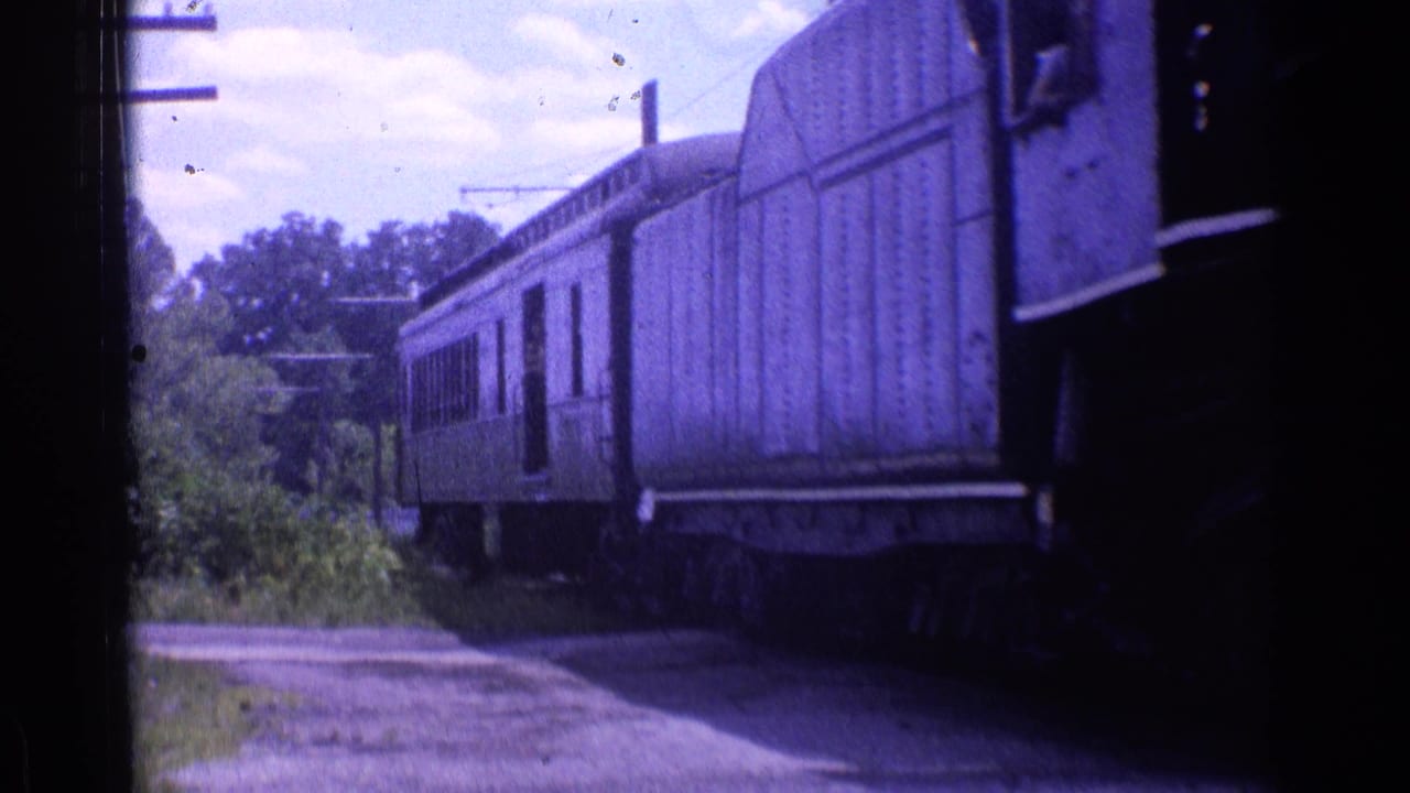 Passenger cars continue past a rural trackside view in 1976 Chicago-area 8mm footage.