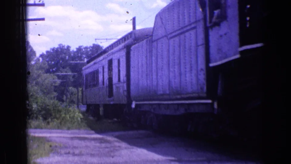 Passenger cars continue past a rural trackside view in 1976 Chicago-area 8mm footage.