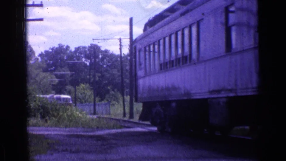 Final 1976 Chicago-area frame of a passenger car rolling past a rural trackside view under a bright sky.