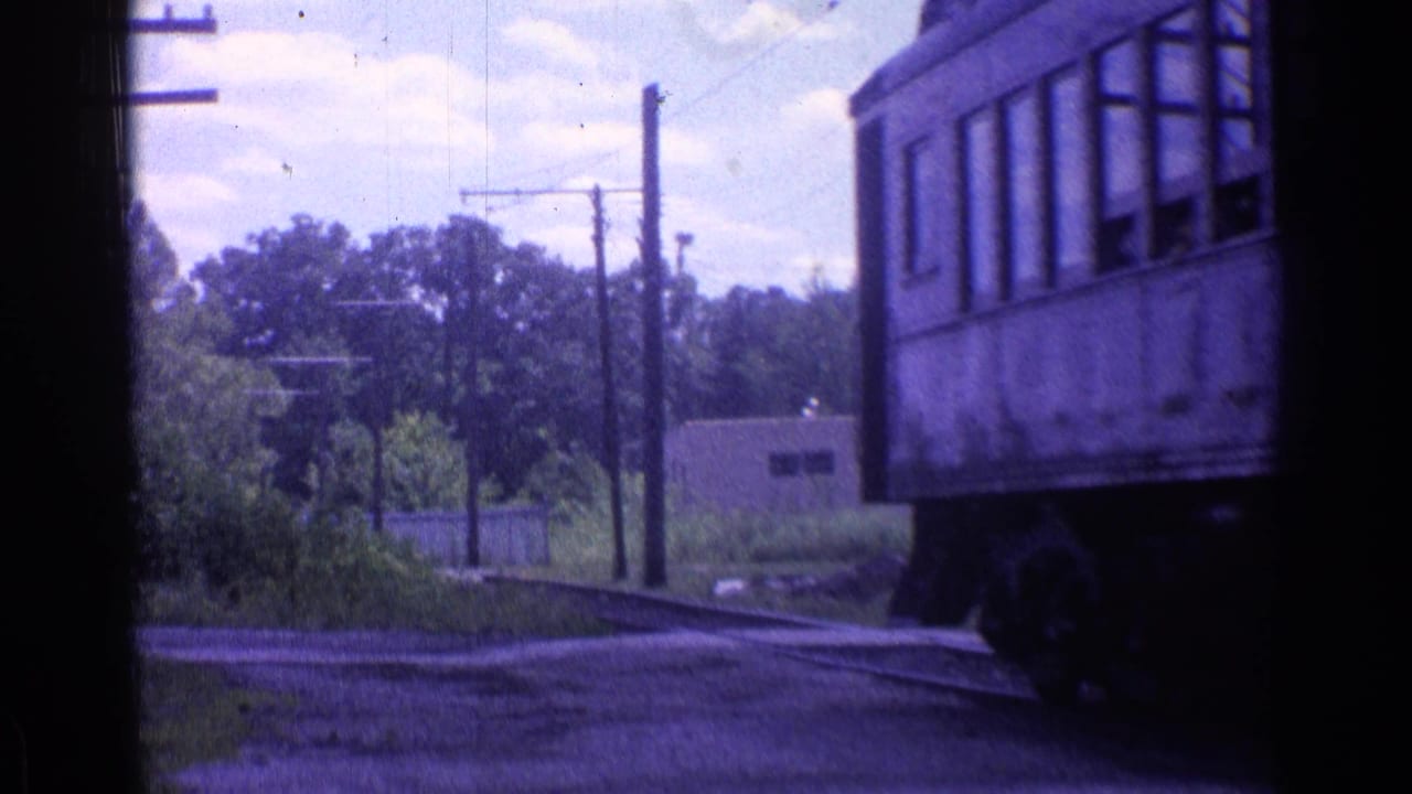 Trackside view with a railcar edge, curving tracks, utility poles, trees, and a low building.