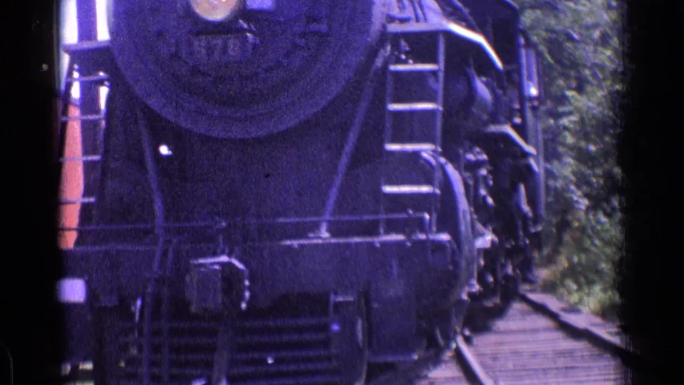 Close 1976 Chicago-area 8mm view of the steam locomotive front, ladder, coupler area, rails, and trees as the engine nears the camera.
