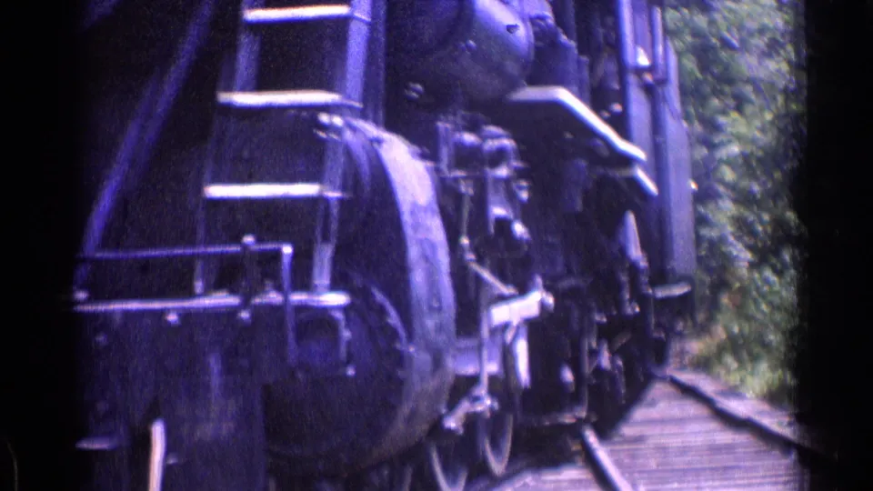 1976 Chicago-area frame showing the steam locomotive passing close by, with ladder, wheel assembly, track, and trees visible in soft 8mm color.
