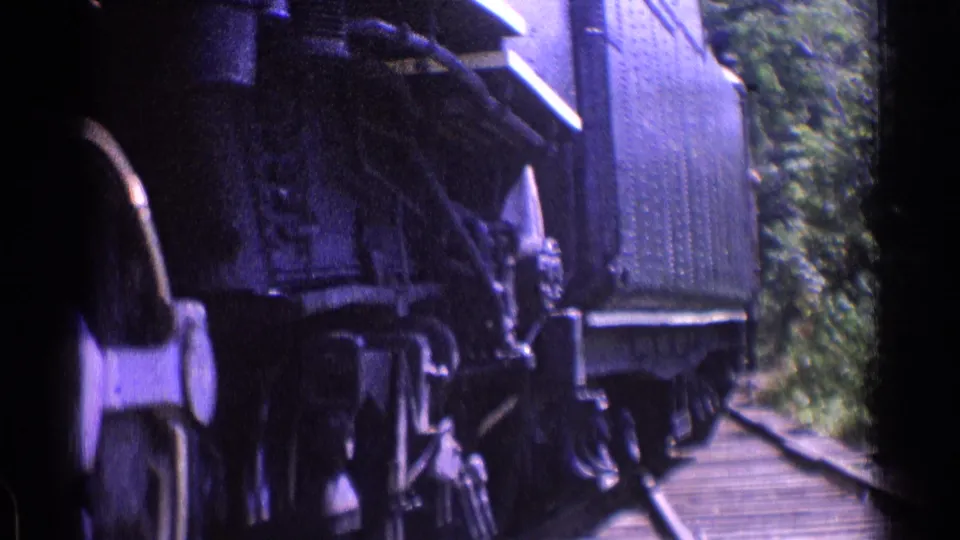 Riveted steam locomotive body and undercarriage pass along wooded tracks in vintage 8mm footage from the reported 1976 Chicago setting.