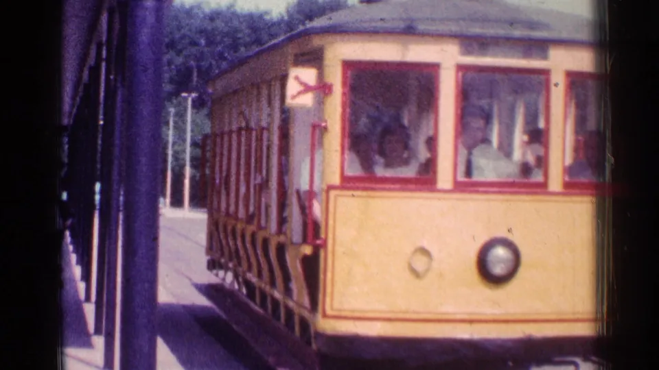 1976 Chicago 8mm frame with a close view of the yellow trolley at the platform, passengers visible through windows and rails below.