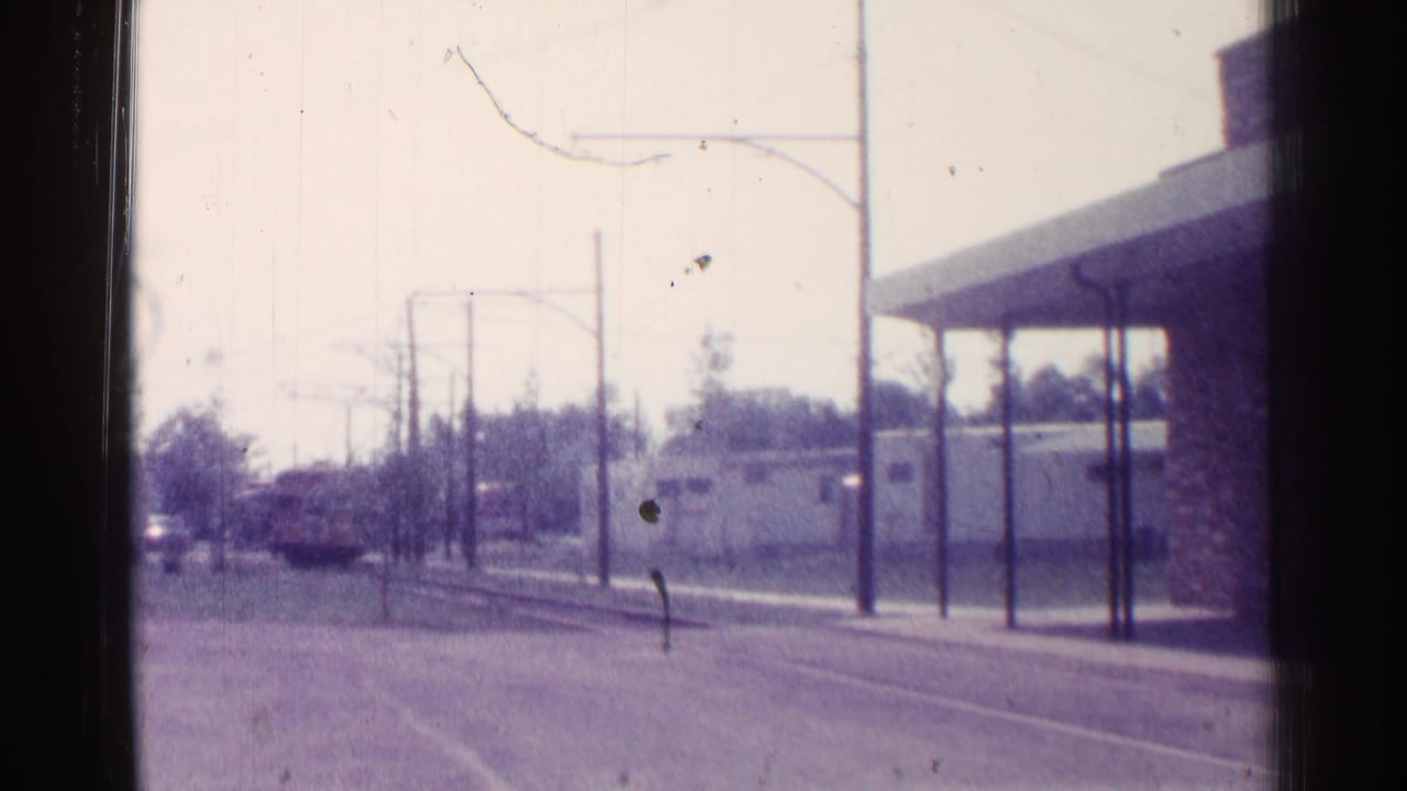 Trolley approaches along street tracks near a canopy and overhead wires.