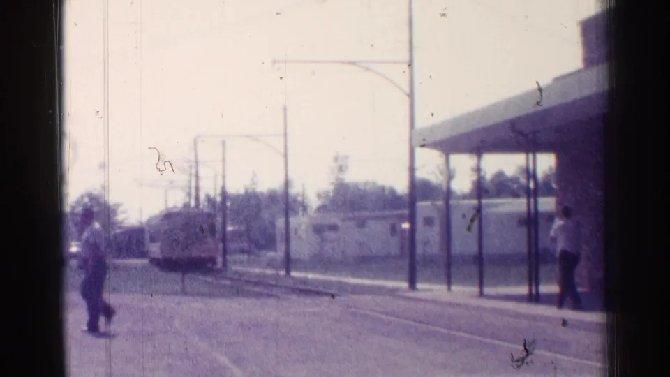 Chicago 1976 street-level transit view with a trolley approaching, a man near the canopy, and another pedestrian near the tracks.
