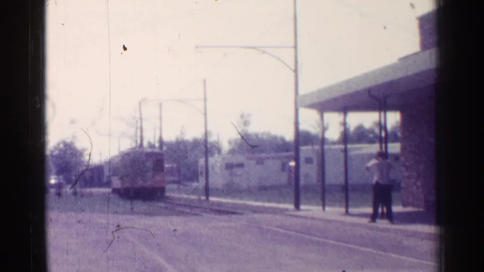 Chicago 1976 8mm frame showing the trolley at the stop area and a man standing on the sidewalk beside the canopy supports.