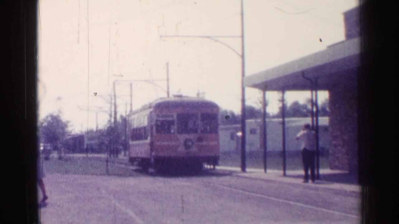 Transit car approaches a curbside stop under overhead wires.