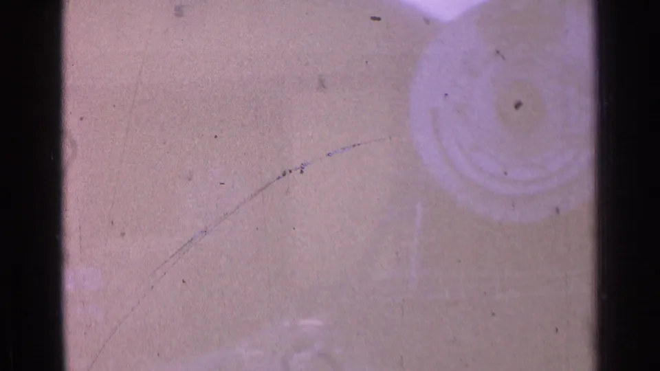 Faded 1976 8mm frame with pink color shift, dust, fine scratches, and a soft circular stain along the right edge.