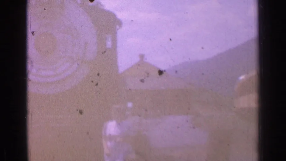 A yellow train car and small distant person appear in a hazy Chicago rail-yard frame from the 1976 8mm footage.
