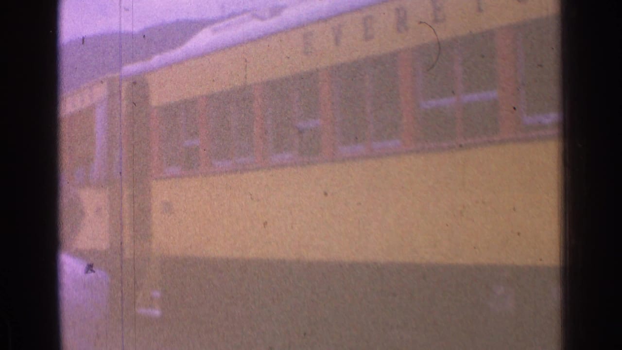 Yellow train car fills the frame with soft hills and sky behind it.