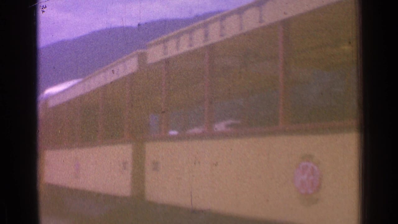 Yellow rail car seen close up with dark window band and hills behind it.