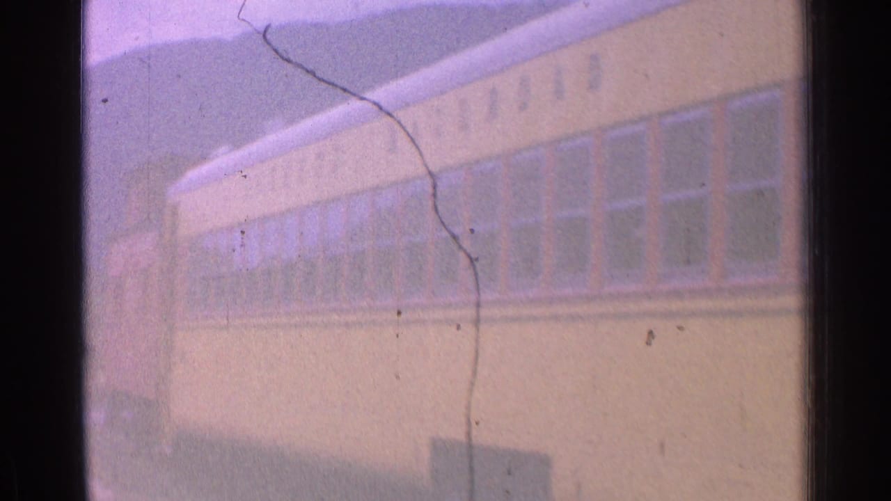 Soft 8mm frame showing the side of a yellow train car, rows of windows, and a faint roofline against a purple-tinted sky.