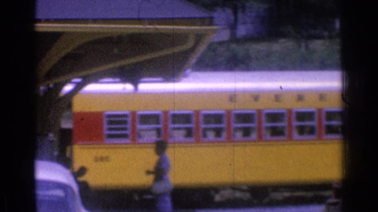 Yellow train car with red window trim passing behind dark foreground framing.