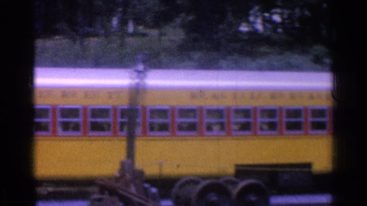Long yellow rail car with red windows and a walking person near the platform.